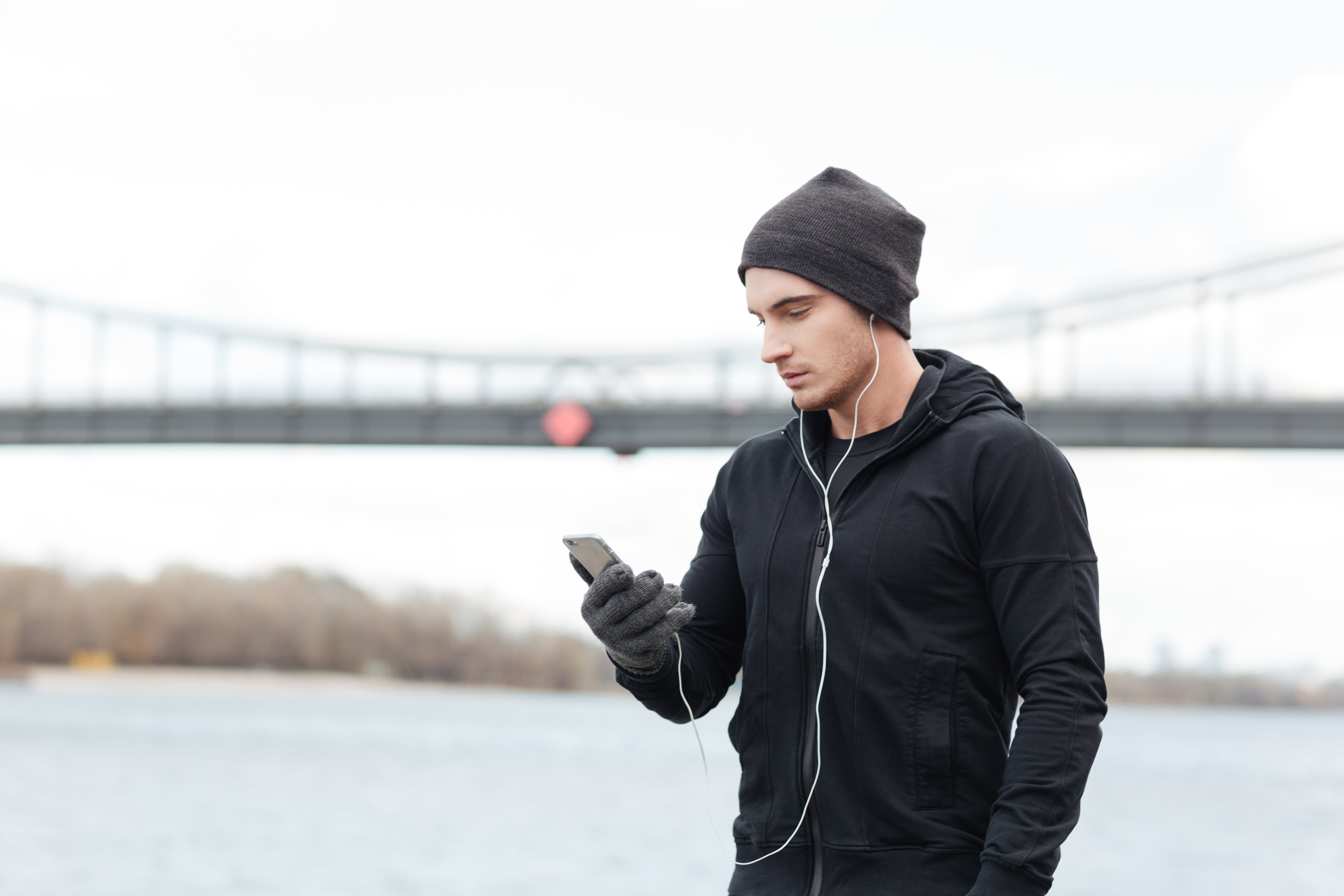 young-man-athlete-in-hat-and-gloves-enjoying-music-with-cell-phone-out