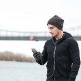 young-man-athlete-in-hat-and-gloves-enjoying-music-with-cell-phone-out